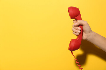 Closeup view of woman holding red corded telephone handset on yellow background, space for text....