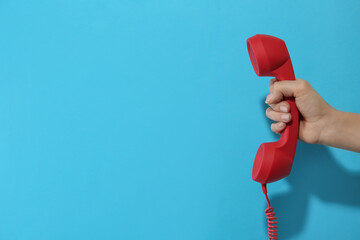 Closeup view of woman holding red corded telephone handset on light blue background, space for...