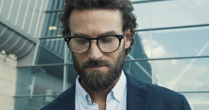 Handsome bearded Startup Businessman in Glasses using mobile Phone. Young man texting Messages, cheating on his Smartphone while walking in Office District. Business. Social Networking. People. Apps.