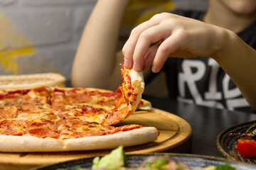 Hand, taking slice of pepperoni pizza from round wooden tray