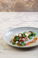 Juicy, appetizing baked eggplant with tomatoes and herbs on a white plate served in a restaurant