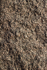 Full frame texture background of a vintage granite stone wall with flecks of beige black and brown colors and rough texture, in natural sunlight