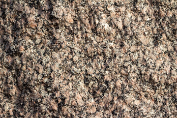 Full frame texture background of a vintage granite stone wall with flecks of beige black and brown colors and rough texture, in natural sunlight