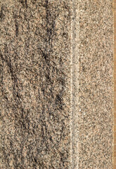Full frame texture background of a vintage granite stone wall with flecks of beige black and brown colors and rough texture, in natural sunlight