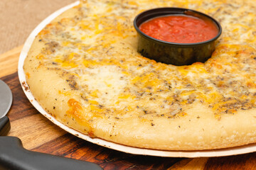 Fresh baked classic cheesy bread topped with herb garlic spread, and cheese blend served with marinara sauce close up on wooden board