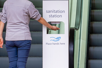 Close-up view of woman sanitizing her hands at sanitation station outside a shopping mall - obrazy, fototapety, plakaty