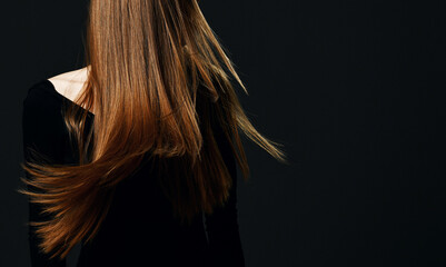 Portrait of young woman standing showing her healthy strong long hair restored after spa procedures treatment over dark background with copy space . Hairstyle. Hair cosmetics