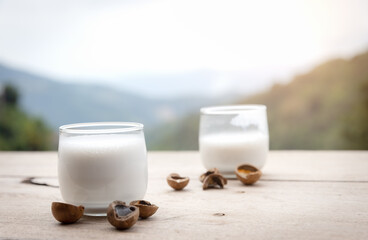 Macadamia milk in a glass with bark on wooden floor and look mountain hill view is background.