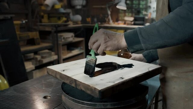 A carpenter paints a piece of wood for a loft-style chair with a brush. Close up