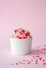 Strawberry ice cream in white ceramic cup with heart topping on pink background