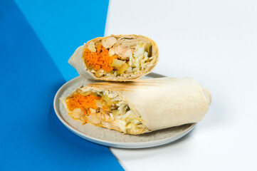 Side view of Chicken meat Shawarma roll with vegetables: cabbage, cucumber, carrot and French fries wrapped in lavash bread served on blue and white abstract background. Street food grilled doner
