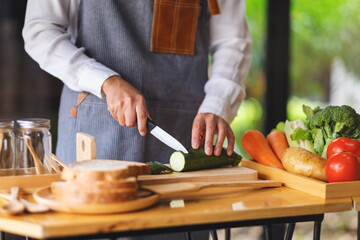Closeup image of a female chef cutting and chopping vegetables by knife on wooden board in kitchen