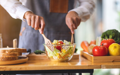 Closeup image of a female chef cooking fresh mixed vegetables salad in kitchen