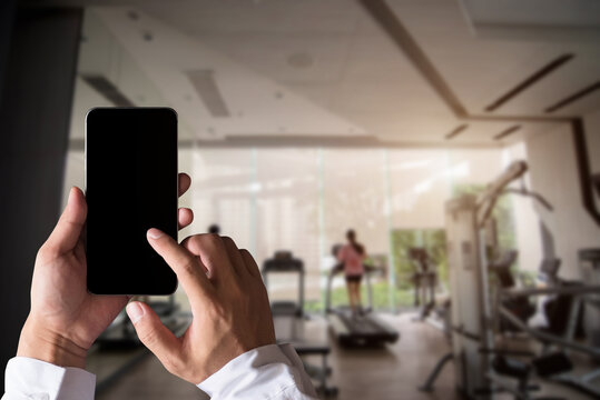 Hand held black phone With a blank white screen in the Gym in the morning light.