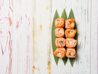 Top view of Delicious Japanese seafood sushi roll with salmon tataki and roasted black tiger shrimps on top served on bamboo leaves on light colorful wooden background. Copy text space. Single object
