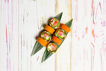 Directly above of Healthy Japanese rice free sushi roll served on bamboo leaves. Raw salmon, tuna, rockfish, avocado, lettuce, cream cheese wrapped in carrot daikon slices on light wooden background
