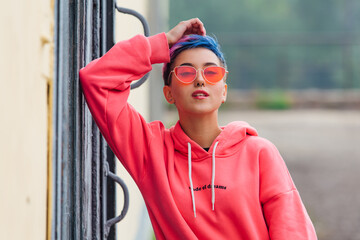 Portrait of a young girl with short colorful hair and nose piercing satanding near the wall with...