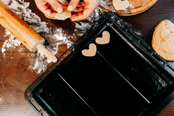 Cookies in shape of heart for the Saint Valentine's Day. Man is baking heart shape cookies for Saint Valentine's Day. Dough, flour, baking pan, round wooden cutting board and rolling pin on the table.