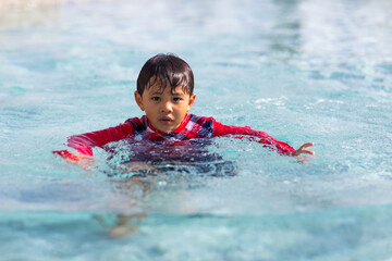 Happy family holiday time. Funny Asian little boy splashing swimming in the pool.