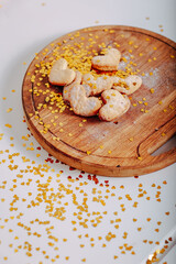 Fototapeta premium Heart-shaped cookies on round wooden cutting board. Saint Valentine's cookies in shape of heart and golden sparkles on white background. Golden glitters in shape of heart on white background.