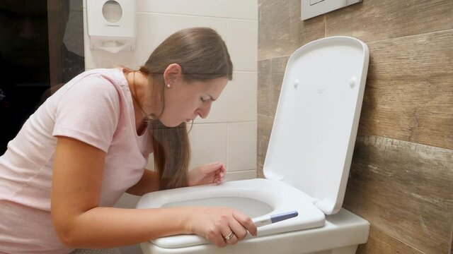 Young pregnant woman vomitting and suffering from nausea in toilet holding positive pregnancy test. Intoxication and nausea during pregnancy