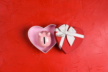 Pink piggy bank in a heart shape gift box on red background.