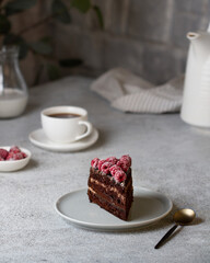 A piece of chocolate cake with raspberries on a gray table, next to tea, dishes.