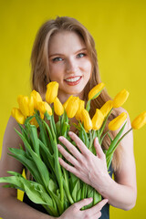 Caucasian woman with an armful of yellow tulips on a yellow background. International Women's Day. Bouquet of spring flowers