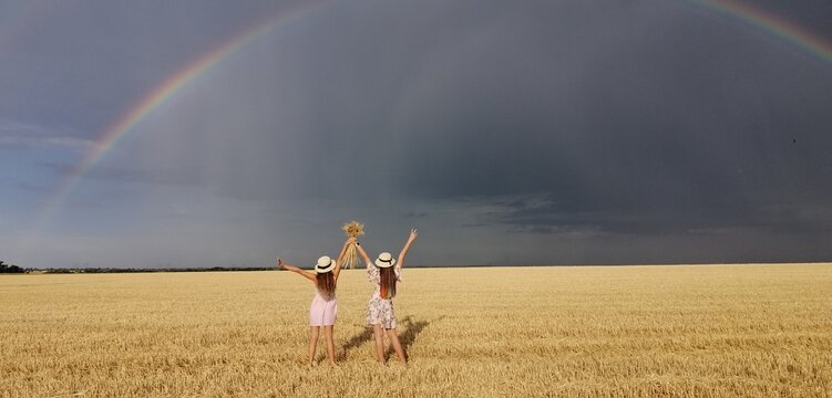 In a wheat field after the rain, two girls run. Colorful real rainbow over the horizon. europe Ukraine. Summer crop fields, ripening wheat field. High quality photo