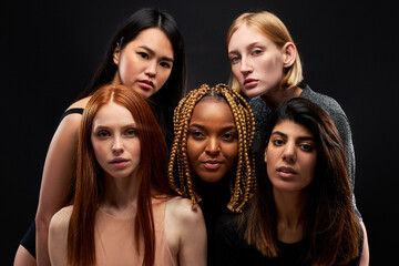 mixed race group of ladies isolated on black background, young women of different ethnicity seriously looking at camera