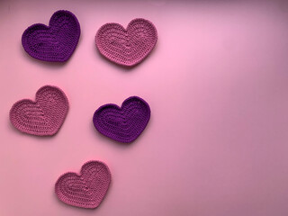 Crochet on the theme of Valentine's Day. In the photo, knitted pink and lilac hearts. Photo from above. The concept of creating a product. Knitted hearts on a pink background.