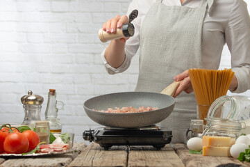 The chef pours spices into frying pan for cooking pasta alla carbonara. Backstage of preparing traditional italian dish on white background. Frozen motion. Cooking process. Cookbook illustration.