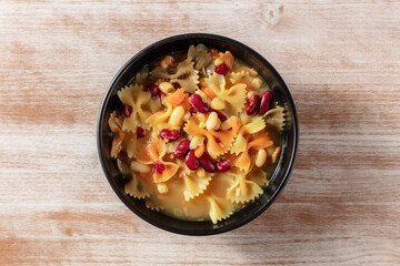 Vegan soup with pasta and beans, overhead shot on a rustic wooden background