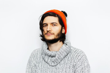 Studio portrait of young guy with orange hat and grey sweater on white background.