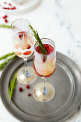 Glasses of champagne cocktail with cranberry and rosemary on light table