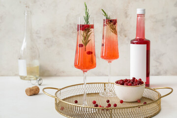 Glass of champagne cocktail with cranberry and rosemary on light table