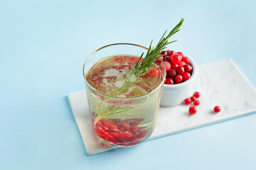 Glass of champagne cocktail with cranberry and rosemary on color background