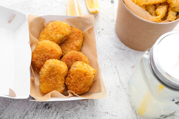 Jar with lemonade, tasty nuggets and french fries in paper box on light background