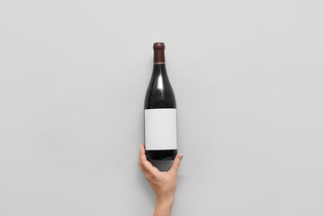 Female hand and bottle of wine with blank label on light  background