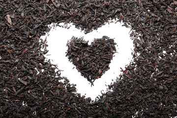 Heart shape made of dry black tea leaves on light background