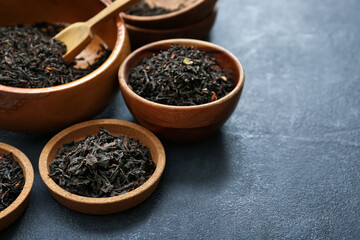 Dry black tea leaves in bowls and scoop on dark background