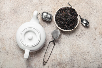 Dry black tea leaves in bowl with infusers and teapot on light background