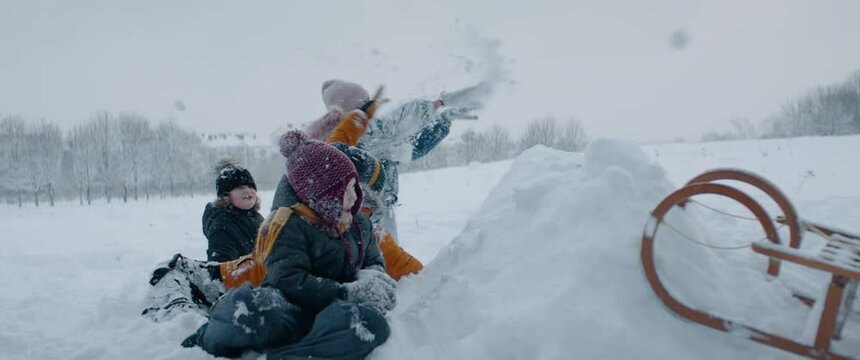 HANDHELD Group of kids having snowball fight brawl, hiding behind the snow fort wall. Fun winter games outside. 120 FPS slow motion shot