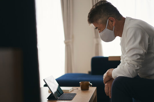 タブレットPCを見るマスクをつけた日本人シニア男性