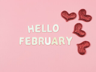 flat lay of wooden letters HELLO FEBRUARY  with red glitter hearts on pink background. Greeting new month and Valentine's day.