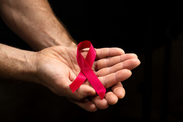 Red ribbon in the hands of a man on a dark background for the concept of World AIDS Day