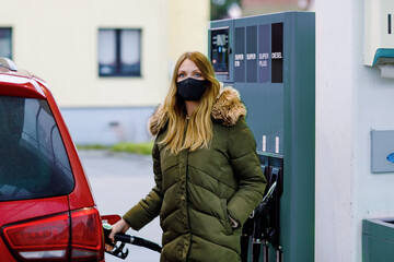 Woman wear medical mask at self-service gas station, hold fuel nozzle, refuel the car with petrol...
