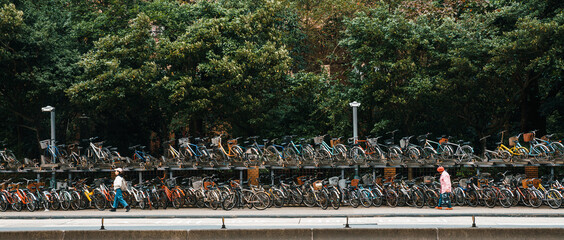 Double-decker bike racks along the sidewalk in front of the National Taiwan University with people walking.