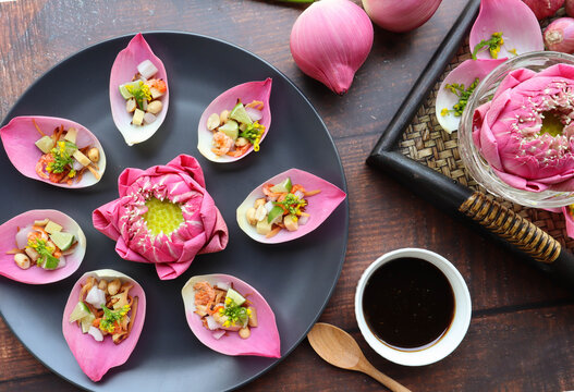 Miang Kham Bua Luang - Pink water lily lotus leaf wrapped with coconut flakes, chopped onion, ginger, chili, dry shrimp and dip with sweet sauce - Authentic Thai appetizer top view on wood table