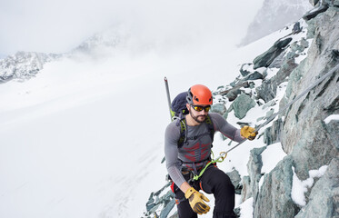 Man alpinist in sunglasses and safety helmet holding fixed rope while climbing snowy mountain....